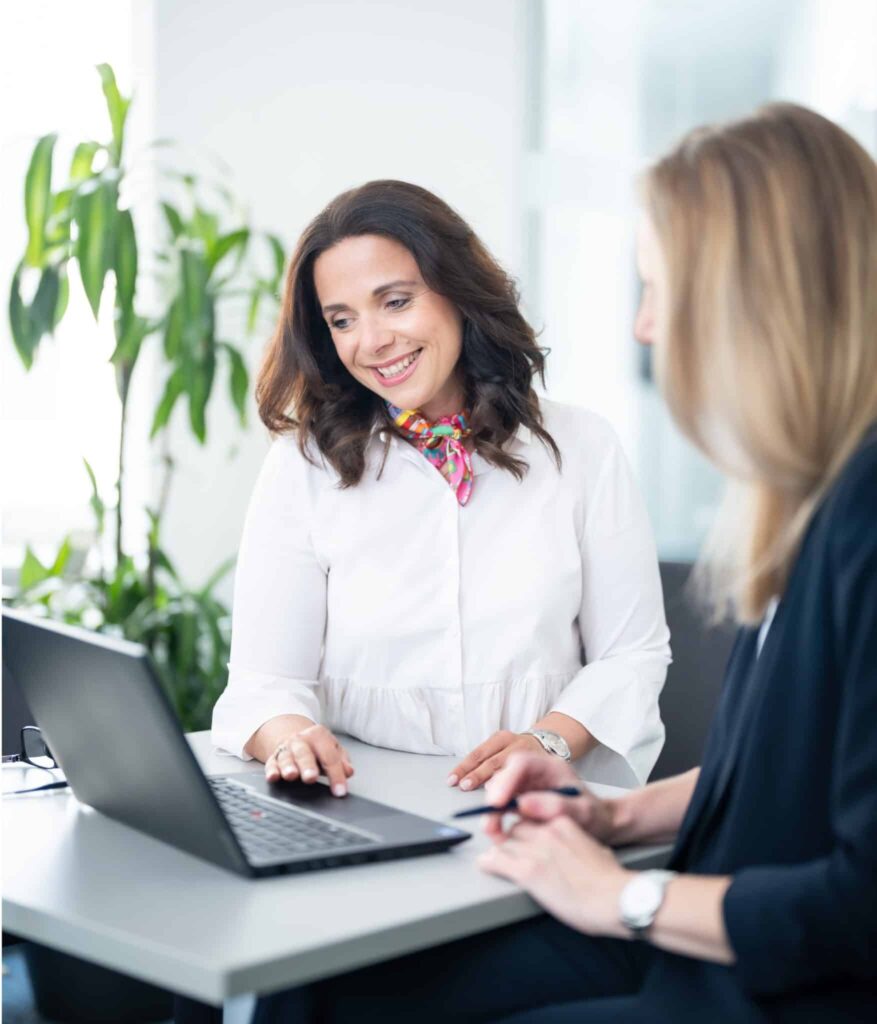 services2-scaled Executive interim management consultant smiling during a business meeting with a colleague beside a laptop.